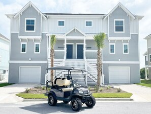 Une maison à deux étages avec un garage, une véranda et un véhicule de golf garé devant.