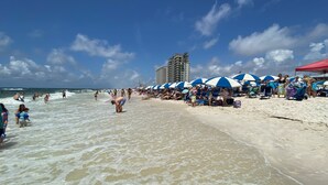 Ein Strand mit Menschen, Sonnenschirmen und einem hohen Gebäude im Hintergrund.