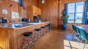 A wooden interior with a kitchen, bar stools, and a dining area with chairs. - Hill Country Barn - Sauna & Cedar Hot Tub (Johnson City)