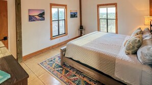 Une chambre avec un plafond en bois, deux fenêtres, un lit avec des oreillers et un tapis.