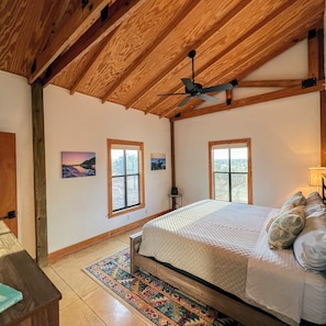 Ein Schlafzimmer mit Holzbalkendecke, zwei Fenstern, einem Bett mit Kissen und einem Teppich.
