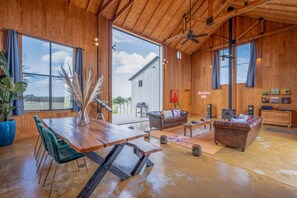 Un salon spacieux avec un plafond en bois, de grandes fenêtres, une table à manger et un coin salon confortable.