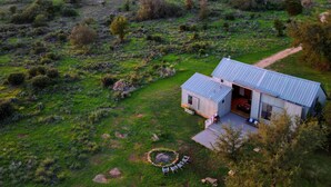 A rustic cabin with a metal roof, surrounded by a lush green landscape and a clear sky. - Hill Country Barn - Sauna & Cedar Hot Tub (Johnson City)