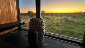 A rustic interior with a stone stove, wooden walls, and a view of a sunset over a grassy field. - Hill Country Barn - Sauna & Cedar Hot Tub (Johnson City)
