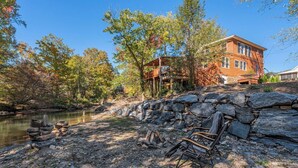 A rustic cabin with a stone foundation, wooden deck, and a river view.