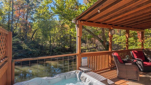 A hot tub on a wooden deck with wicker chairs and a view of a forested area.