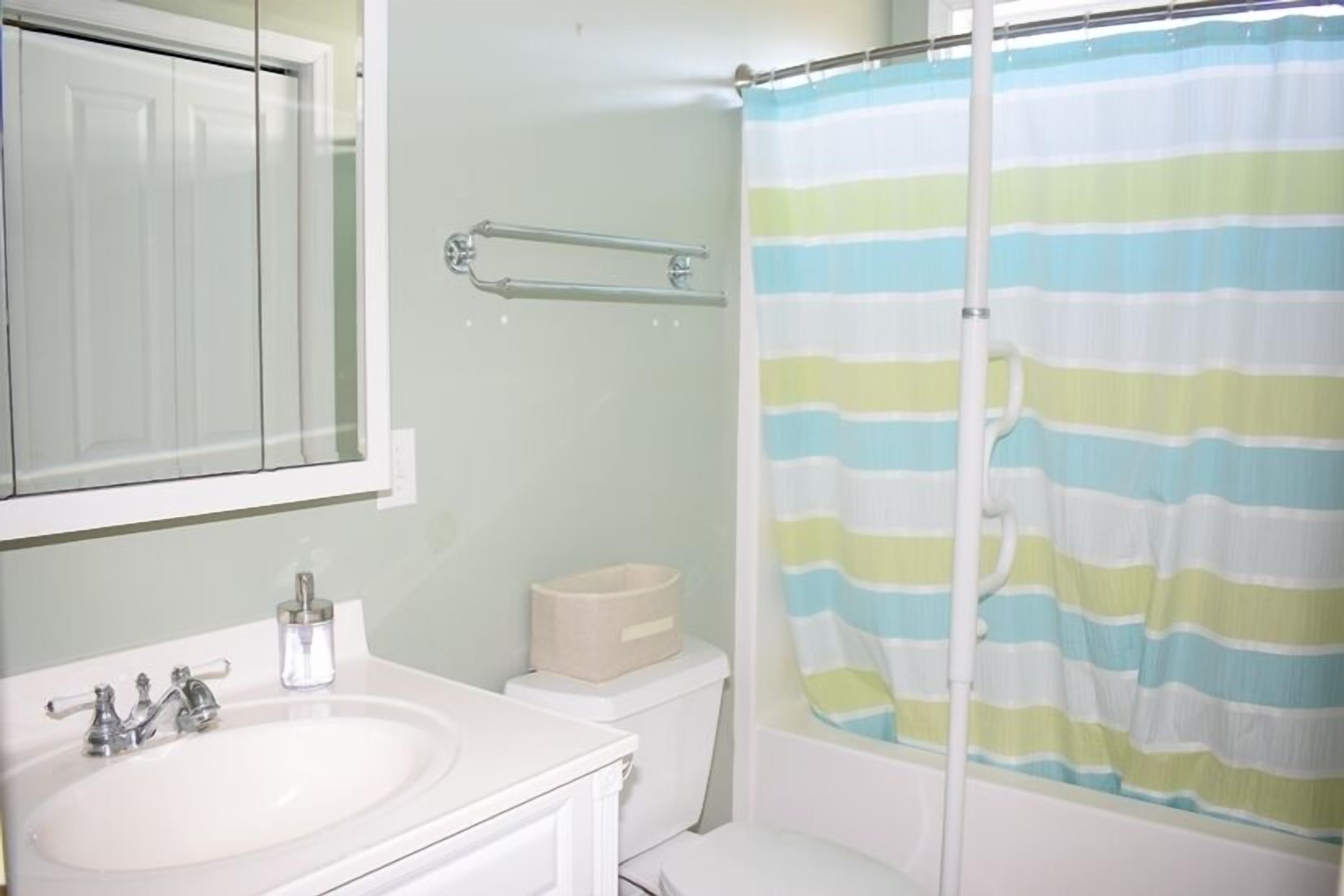 A bathroom with a white sink, a mirror, a toilet, and a shower curtain with horizontal stripes.