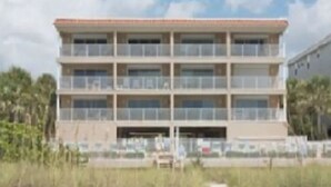Ein mehrstöckiges Hotel mit Balkonen in Strandnähe, mit Palmen.