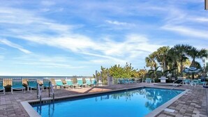 Ein rechteckiger Pool mit Tiefenhinweisschild für 1,50 Meter, umgeben von einer Ziegelterrasse und grünen Liegestühlen.