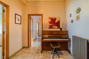 A hallway with a grand piano, a framed picture on the wall, and a large floral artwork.