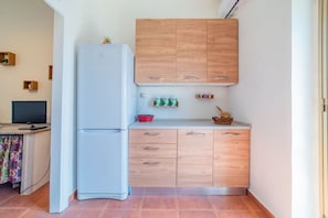 A compact kitchen with a white refrigerator, wooden cabinets, a small countertop, and a television on a desk.