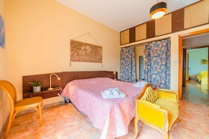 A bedroom with a bed, a chair, a desk, a mirror, and a hanging tapestry.