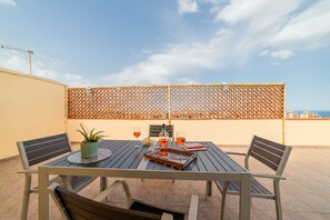 A rooftop terrace with a table set for two, a potted plant, and a bottle of wine. - GuestHost - Roomy and bright apartment of 150 sqm, with two balconies and a panoramic terrace of 150 sqm with views of Syracuse, Ortigia and the sea. The flat can accommodate up to 5 people and is located on the 5th floor of a building with lift, in a re (Siracusa)