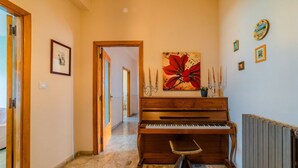 A hallway with a grand piano, a framed picture on the wall, and a large floral artwork. - GuestHost - Roomy and bright apartment of 150 sqm, with two balconies and a panoramic terrace of 150 sqm with views of Syracuse, Ortigia and the sea. The flat can accommodate up to 5 people and is located on the 5th floor of a building with lift, in a re (Siracusa)
