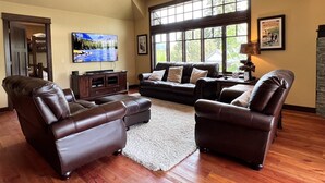 A spacious living room with leather sofas, a flat-screen TV, and large windows offering a view of the outdoors. - Rs156 Downtown Whitefish Experience (Whitefish)