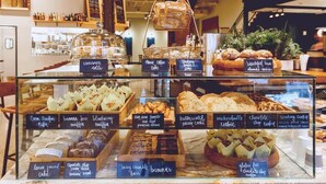 A bakery display case with various baked goods labeled, including cinnamon rolls, coffee cake, and chocolate chip cookies.