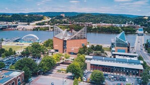 An aerial view of a cityscape with a prominent building with a unique triangular roof structure, a body of water, and a bridge in the background.