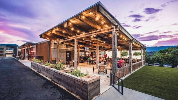 A covered outdoor seating area with tables and chairs, surrounded by a wooden deck and a grassy lawn.