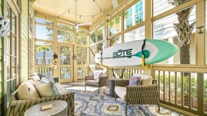 Une véranda ensoleillée, dotée de sièges confortables, d’une planche de surf et offrant une vue sur l’extérieur.