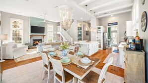 Un salon spacieux avec une cheminée, un coin repas avec une table en bois et une cuisine avec des meubles blancs.