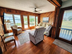 A room with wooden flooring, a ceiling fan, a sofa, a chair, a table, and a view of a lake through large windows. - Great Blue- 3 BR I Waterfront with Private Pier & Boat Dock (Chincoteague)