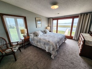 Un dormitorio con cama, una silla, cómoda, lámpara y ventana con vista al agua.