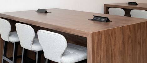 A conference table with four grey upholstered chairs and a black electronic device on it.