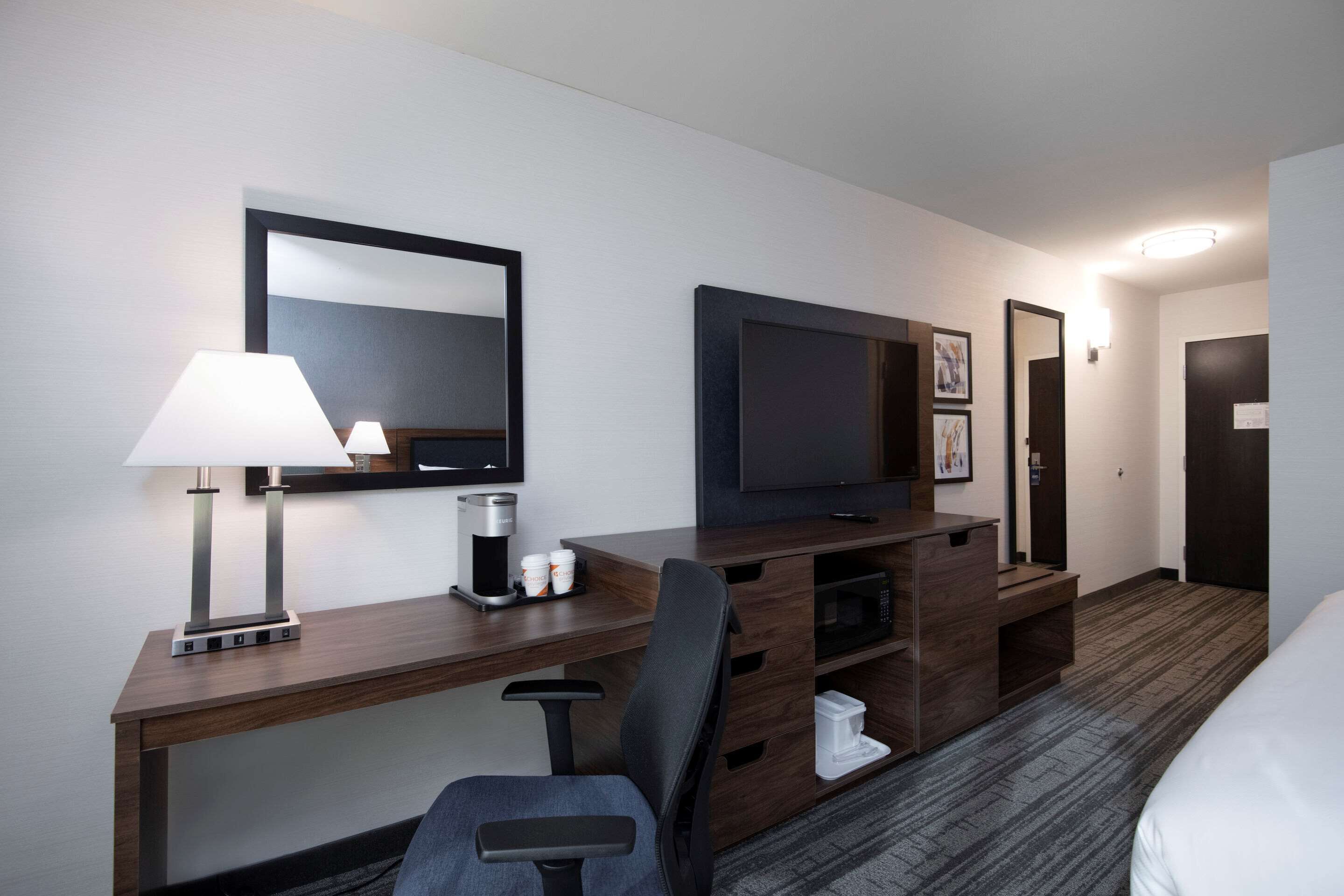 A hotel room with a wooden desk, a chair, a television, a coffee maker, and a bed.