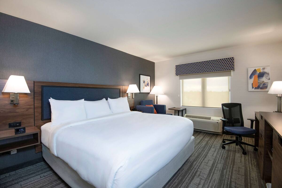Ein Hotelzimmer mit einem großen Bett, zwei Nachttischen mit Lampen, einem Schreibtisch, einem Stuhl und einem Fenster mit Blick.