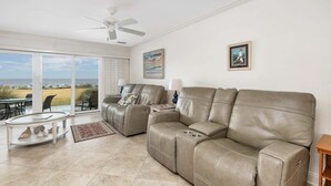 A living room with a beige leather sofa, a glass coffee table, and a ceiling fan.
