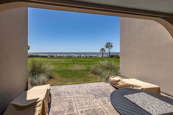 A patio with a view of the beach, covered seating, and a stone-tiled floor. - 1112 Beachview Drive (Saint Simons Island)