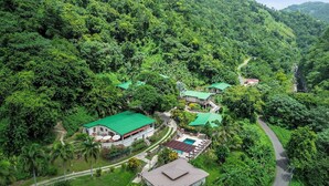 A lush, green landscape with a series of buildings featuring green roofs, surrounded by dense vegetation and a winding road. - Casa Grande Mountain Retreat - Adults Only (Utuado)
