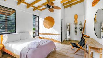 Een slaapkamer met een bed, een plafondventilator van hout, een ronde spiegel en een houten tafel.