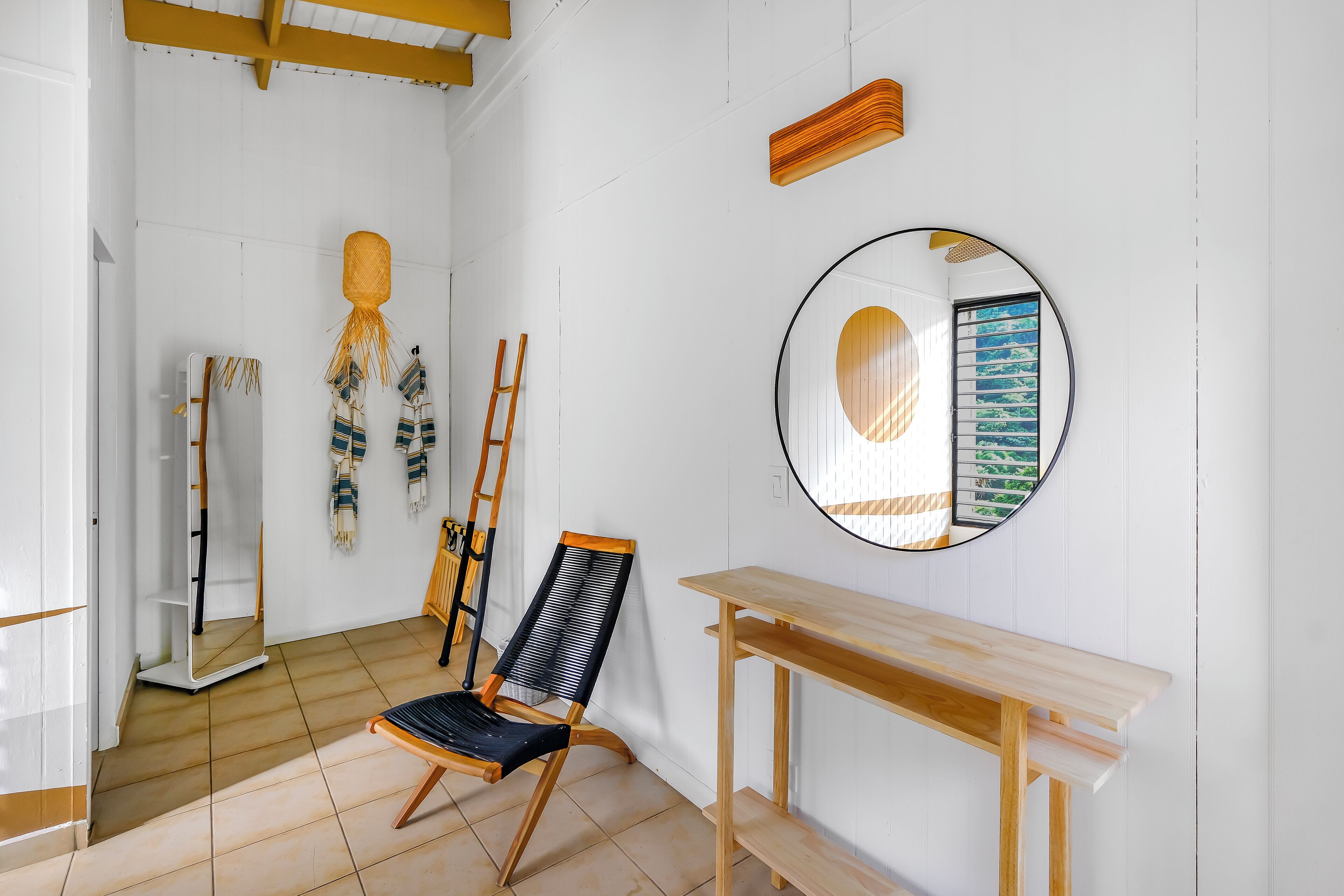 A room with a wooden chair, a round mirror, and a wooden table.