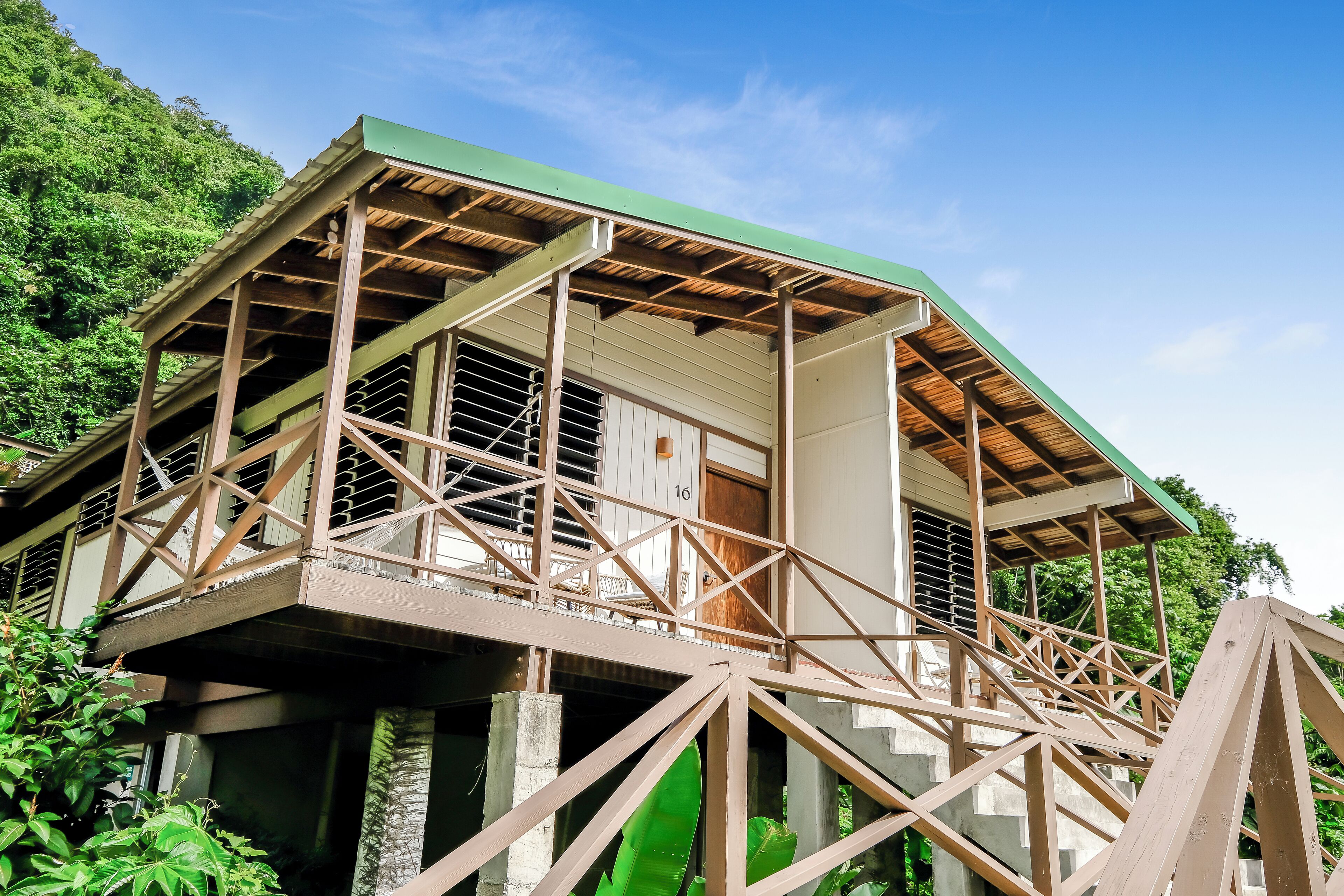 A two-story wooden structure with a balcony, elevated on stilts, surrounded by lush greenery.