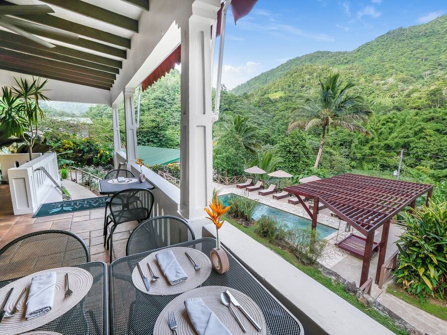 A terrace with tables set for dining, overlooking a lush green landscape and a pool.