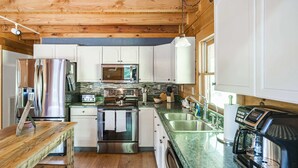 A modern kitchen with stainless steel appliances, white cabinets, and a wooden dining table. - Hillside Haven | Luxe Hot Tub | Cornhole | Jenga (Whitwell)