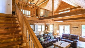 A wooden cabin interior with a staircase, leather couches, and a dining area. - Hillside Haven | Luxe Hot Tub | Cornhole | Jenga (Whitwell)
