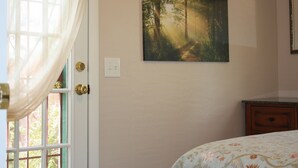 Ein Schlafzimmer mit einem Bett, einem Fenster mit Vorhängen, einem Waldgemälde und einem Nachttisch aus Holz.