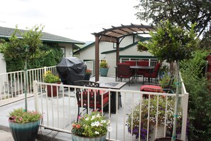Eine Terrasse im Freien mit überdachter Sitzgruppe, Topfpflanzen und einem Grill.