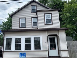 A two-story house with a garage door, a front door with a number, and a sign for seasonal rentals.