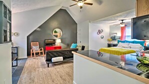 A modern loft-style bedroom with a sloped ceiling, a black bed, a small desk, and a seating area with a sofa and chairs. - Bright Lakeside Studio - Hike, Fish, and Bike! (Golden)