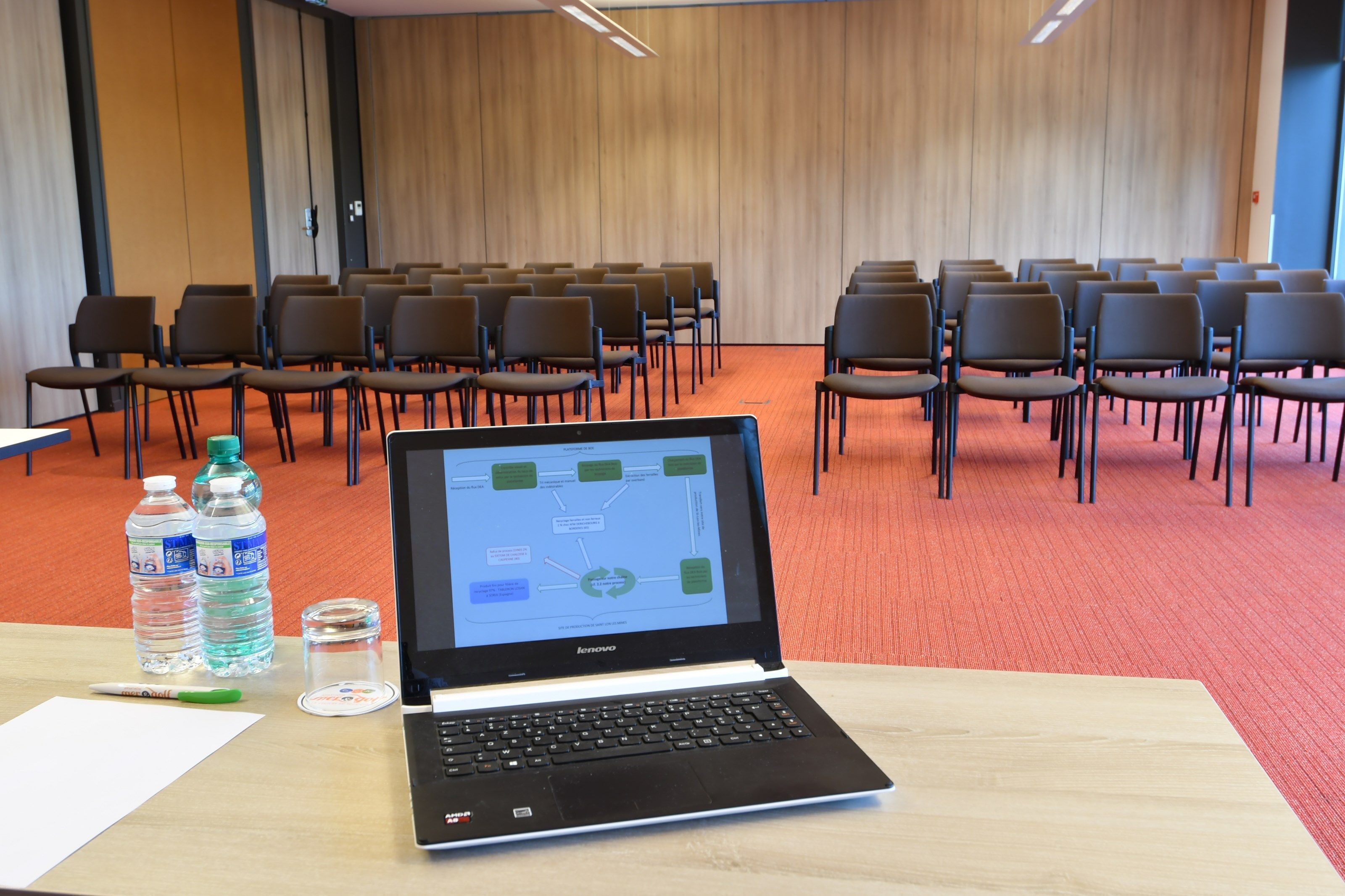 A conference room with rows of chairs, a laptop on a table, water bottles, and a glass.