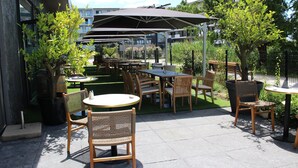 Una terrazza esterna con tavoli e sedie, circondata da vegetazione e un edificio sullo sfondo.