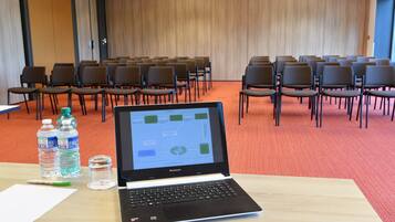 Ein Konferenzraum mit Stuhlreihen, einem Laptop auf einem Tisch, Wasserflaschen und einem Glas.