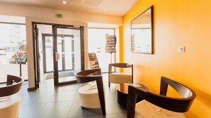 A reception area with a modern design, featuring a bright yellow wall, a reception desk, and a seating area with chairs and a small table. - Bon Rapport Qualité-Prix! Studio Equipé + Parking (Perpignan)