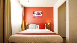 A hotel room with a bed, two bedside lamps, a painting on the wall, and a door to the right. - Bon Rapport Qualité-Prix! Studio Equipé + Parking (Perpignan)