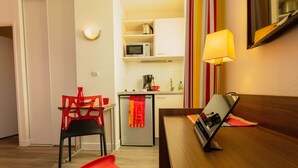 A compact living space with a kitchenette, a dining area with a red chair, and a bed with a bedside table. - Bon Rapport Qualité-Prix! Studio Equipé + Parking (Perpignan)