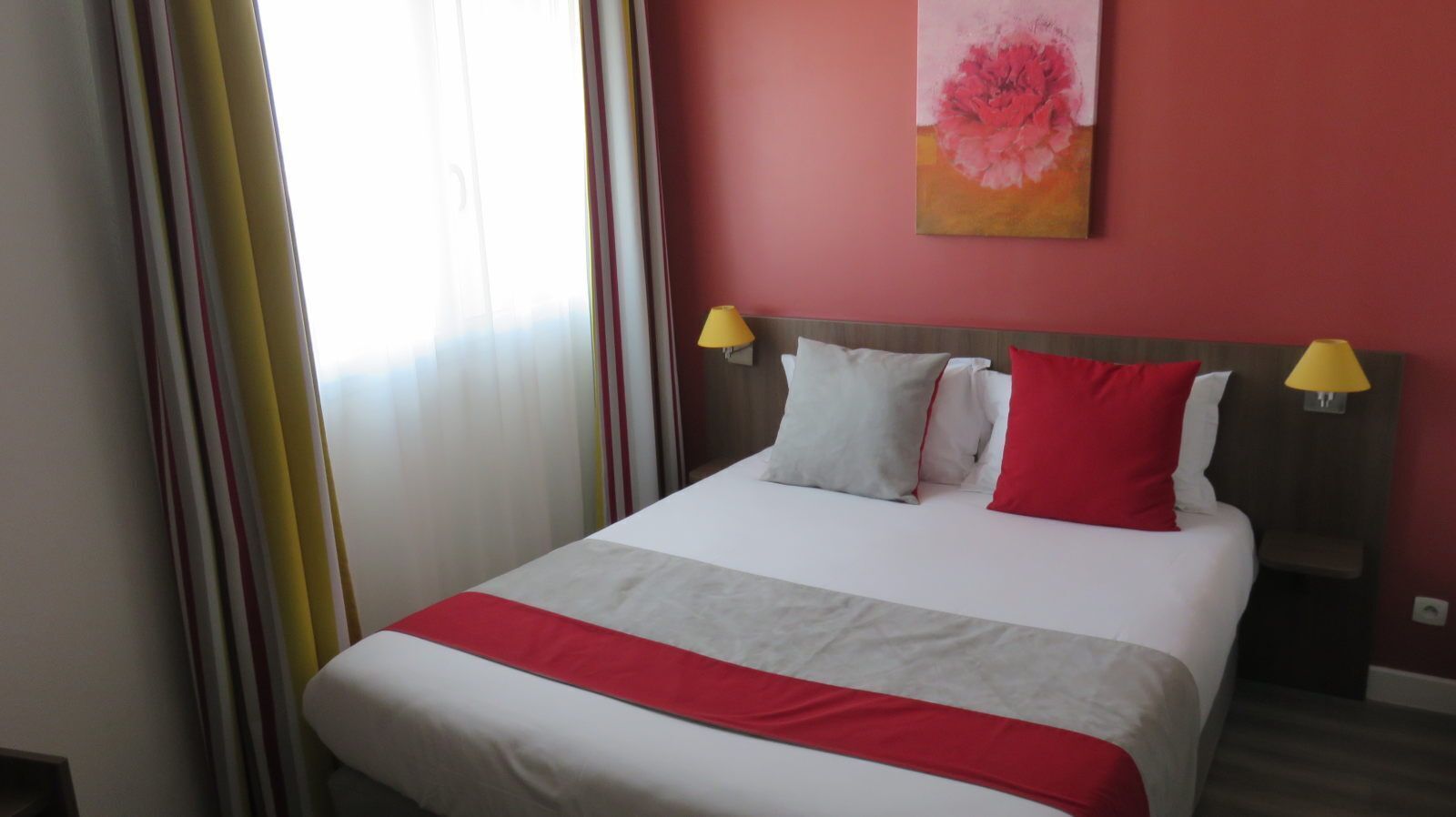 Een hotelkamer met een bed, gordijnen, een schilderij en twee bedlampen.