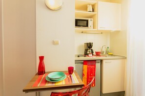 Una cocina compacta con microondas, cafetera y un pequeño comedor con mesa y sillas.